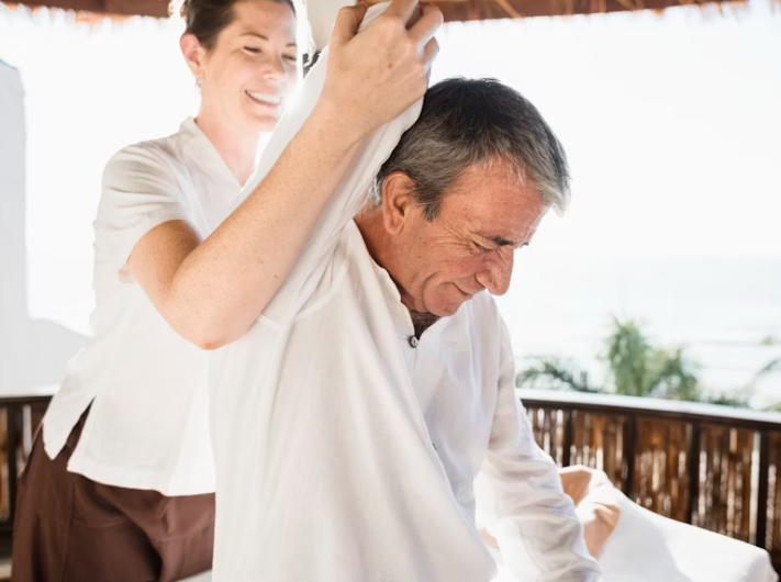 Imagem de destaque do blog. Mãos de um terapeuta tocando gentilmente o ombro de uma pessoa idosa, simbolizando a massagem tântrica para a terceira idade.