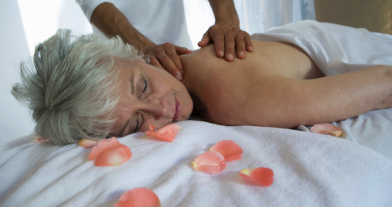 Pessoa idosa confortavelmente posicionada em uma maca de massagem com apoios, destacando as adaptações técnicas para a segurança e o conforto.